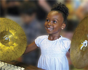 Young girl at the Instrument Petting Zoo playing with cymbals and has a big smile on her face